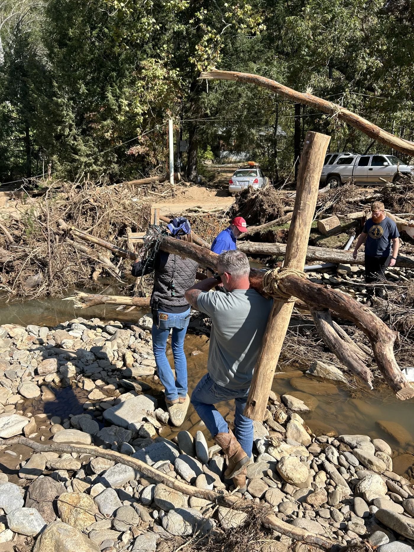 Volunteers carrying a wooden cross through storm debris along a creek